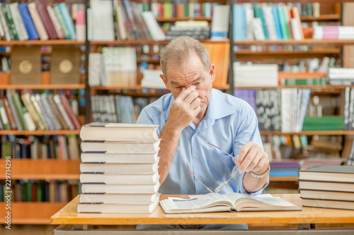 Tired senior man having a headache in library photo