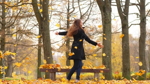 Happy woman dancing in park and throwing yellow leaves in air photo