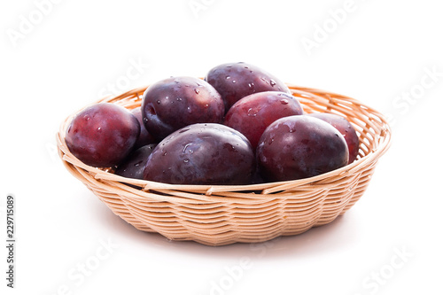 Yellow wooden basket with ripe plums isolated on a white background..