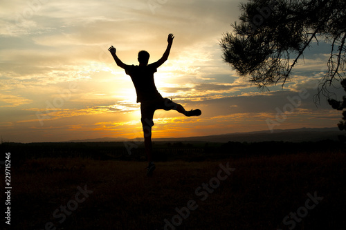 backlight of a man jumping in a pine forest at sunset