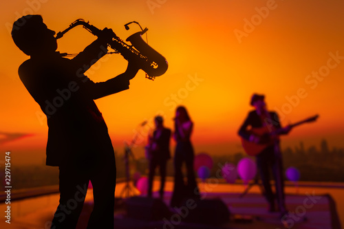 Photography Silhouette saxophone musician man showing with blurry jazz trio band and twilight cityscape background