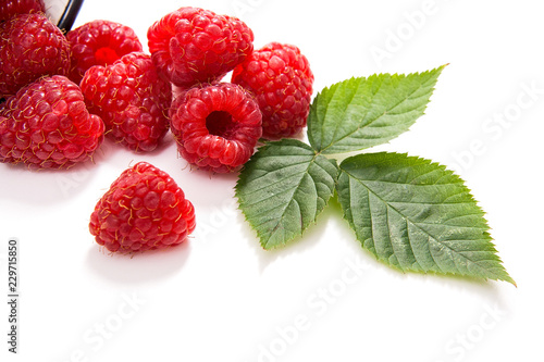 White cup with ripe raspberries and green leaf isolated on white background.