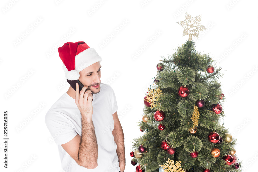 man in santa claus hat talking on smartphone near christmas tree isolated on white man in santa claus hat talking on smartphone near christmas tree isolated on white