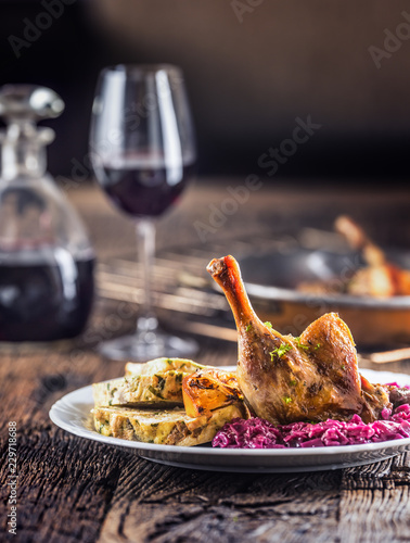 Portion of roast duck leg red cabbage homemade dumplings on plate and red wine on the background photo