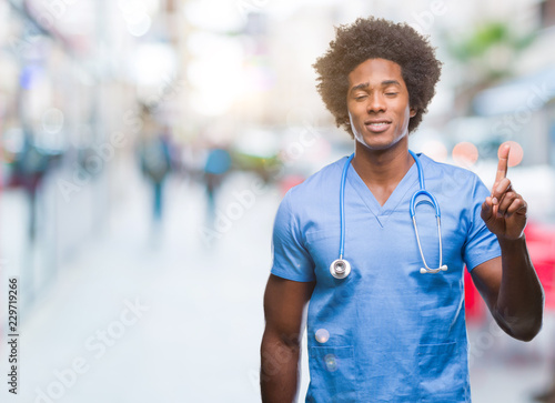 Afro american surgeon doctor man over isolated background showing and pointing up with finger number one while smiling confident and happy.