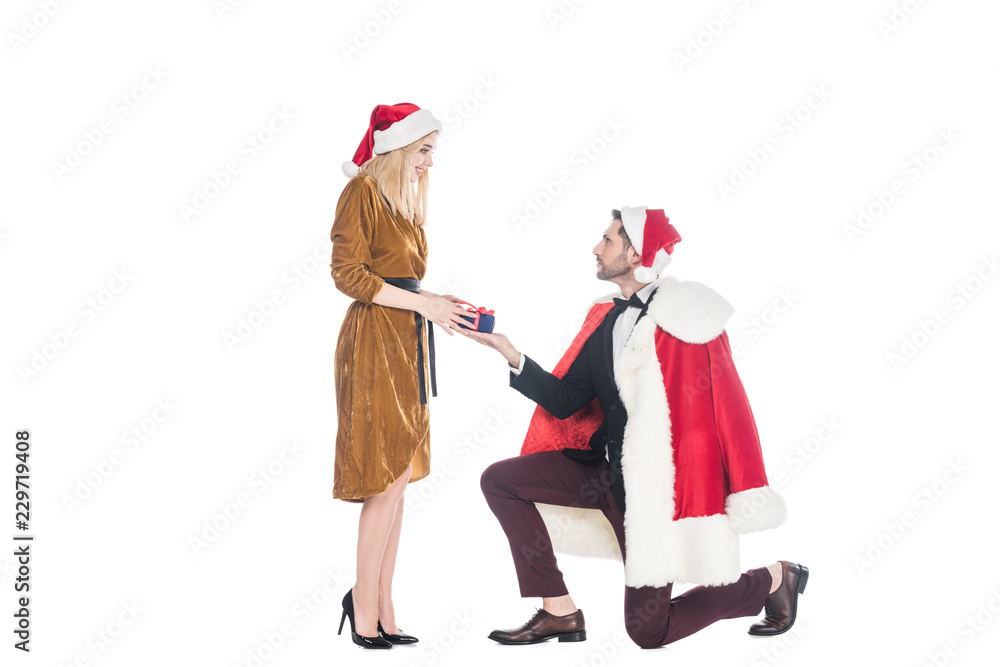 man in santa claus costume presenting gift to girlfriend in santa claus hat isolated on white
