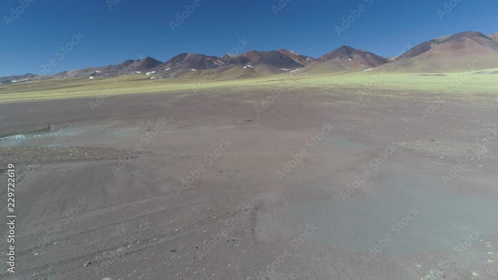 Aerial drone scene of van traveling over road between rocky eroded colorfull mountains with yellow vegetation in front. Catamarca, Argentina. General view of landscape. Aerial drone scene of van traveling over road between rocky eroded colorfull mountains with yellow vegetation in front. Catamarca, Argentina. General view of landscape.