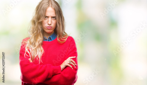 Beautiful young blonde woman wearing winter sweater over isolated background skeptic and nervous, disapproving expression on face with crossed arms. Negative person.