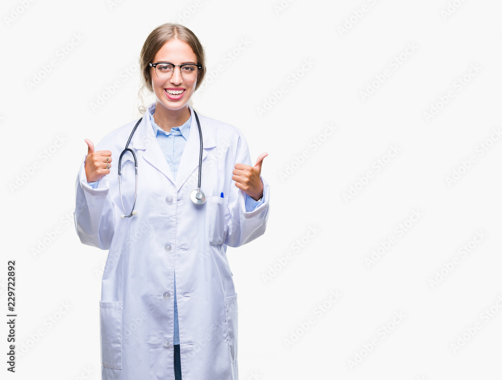Beautiful young blonde doctor woman wearing medical uniform over isolated background success sign doing positive gesture with hand, thumbs up smiling and happy. Looking at the camera Beautiful young blonde doctor woman wearing medical uniform over isolated background success sign doing positive gesture with hand, thumbs up smiling and happy. Looking at the camera