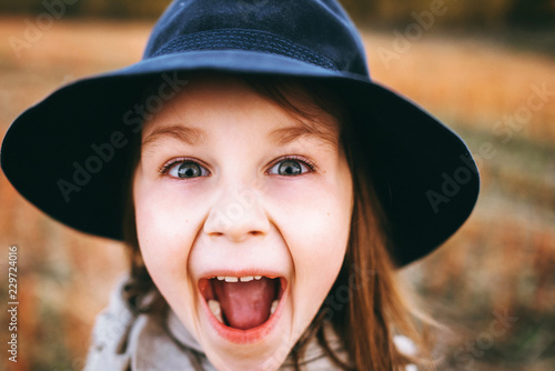 Very emotional autumn portrait of a cute little girl in a field near the forest. Atmospheric autumn background. Little cute girl in a poncho and a hat in a field with several leaves in her hand. 