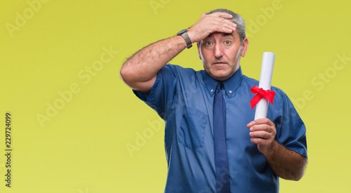 Handsome senior man holding degree over isolated background stressed with hand on head, shocked with shame and surprise face, angry and frustrated. Fear and upset for mistake.