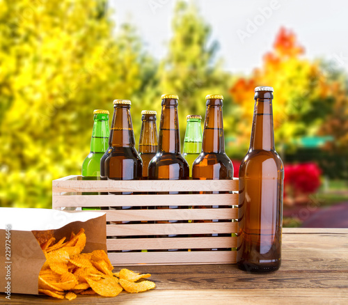 Fototapeta Naklejka Na Ścianę i Meble -  beer bottles and potato chips on wooden table with blurred forrest on background,coloured bottle, food and drink concept,selective focus,copy space