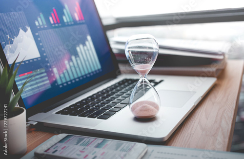 Business concepts with businessman holding hourglass with graph chart on computer laptop