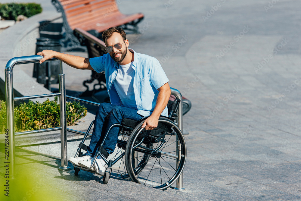 handsome man in sunglasses using wheelchair on stairs without ramp and looking at camera