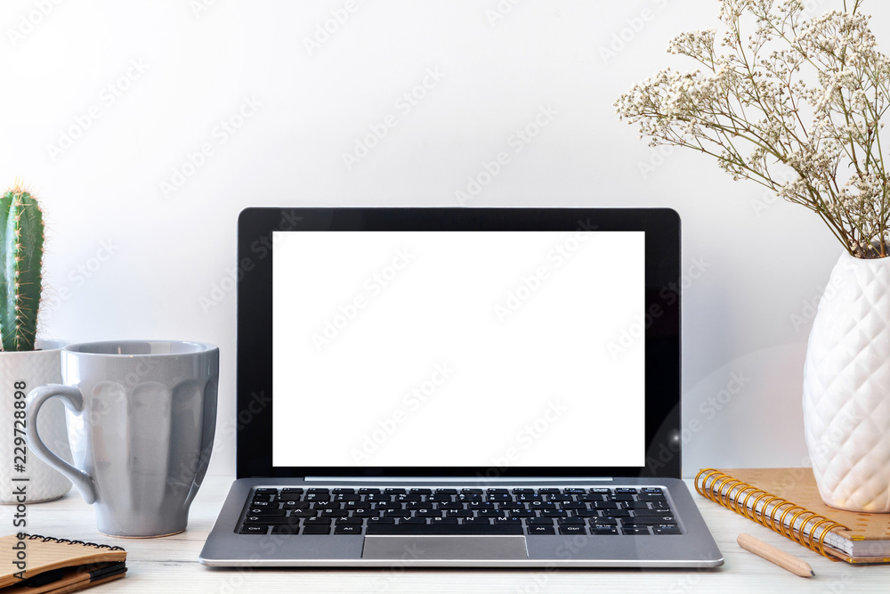Fototapeta premium Hipster wooden desk with an open laptop mockup, a white vase with dried flowers, a notebook, a notebook, a gray cup of coffee and a cactus