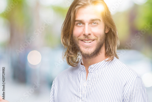 Young handsome man with long hair over isolated background amazed and smiling to the camera while presenting with hand and pointing with finger.