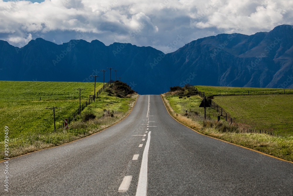 Road through agricultural fields with mountain range in the distance - Somerset West, Western Cape, South Africa.
