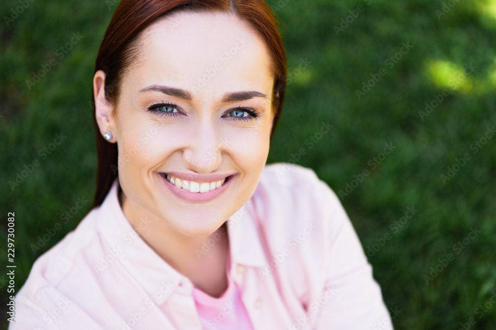 head and shoulders of attractive happy redhair woman in pink shirt looking at camera in park head and shoulders of attractive happy redhair woman in pink shirt looking at camera in park