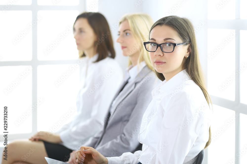 Obraz premium Atrakcyjna bizneswoman na spotkaniu lub konferencji na tle kolegów. Grupa ludzi biznesu w pracy. Portret prawnika lub sekretarza
