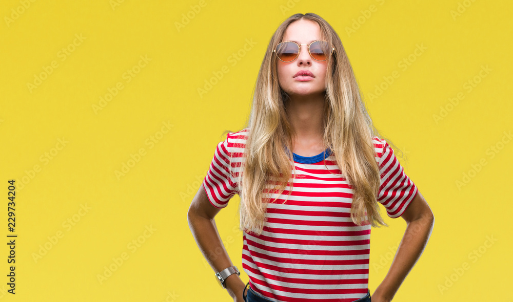 Young beautiful blonde woman wearing sunglasses over isolated background with serious expression on face. Simple and natural looking at the camera. Young beautiful blonde woman wearing sunglasses over isolated background with serious expression on face. Simple and natural looking at the camera.