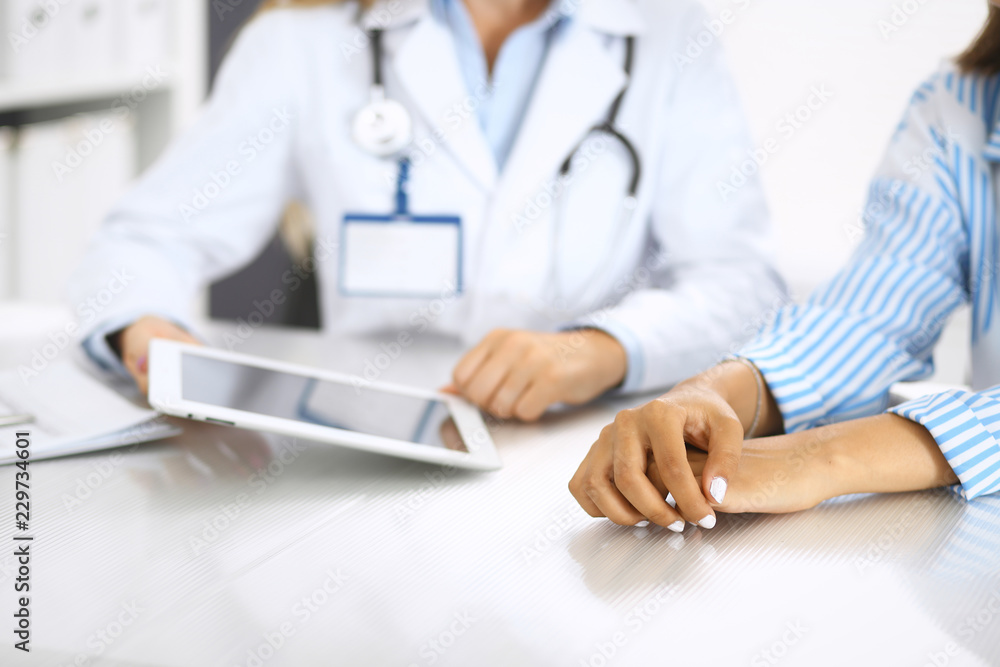 Doctor and patient talking and discussing health treatment while sitting at the desk. Physician pointing into tablet pc, close-up. Medicine and health care concept Doctor and patient talking and discussing health treatment while sitting at the desk. Physician pointing into tablet pc, close-up. Medicine and health care concept