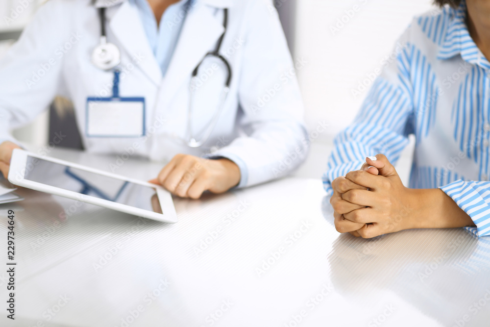 Doctor and patient talking and discussing health treatment while sitting at the desk. Physician pointing into tablet pc, close-up. Medicine and health care concept Doctor and patient talking and discussing health treatment while sitting at the desk. Physician pointing into tablet pc, close-up. Medicine and health care concept