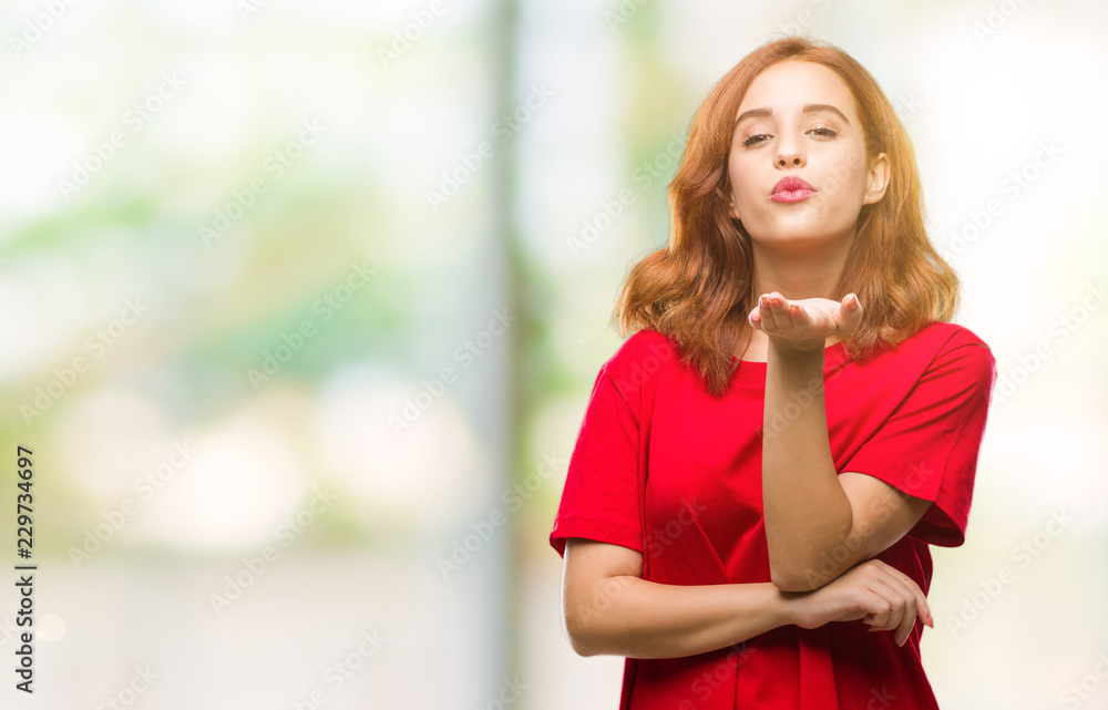 Young beautiful woman over isolated background looking at the camera blowing a kiss with hand on air being lovely and sexy. Love expression.