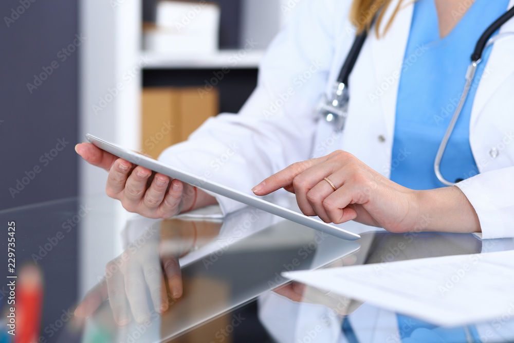 Woman doctor using tablet computer while standing straight in hospital office, closeup. Healthcare, insurance and medicine concept Woman doctor using tablet computer while standing straight in hospital office, closeup. Healthcare, insurance and medicine concept