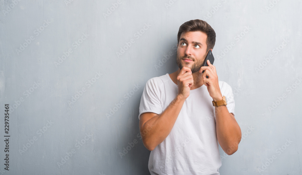 Handsome young man over grey grunge wall speaking on the phone serious face thinking about question, very confused idea Handsome young man over grey grunge wall speaking on the phone serious face thinking about question, very confused idea