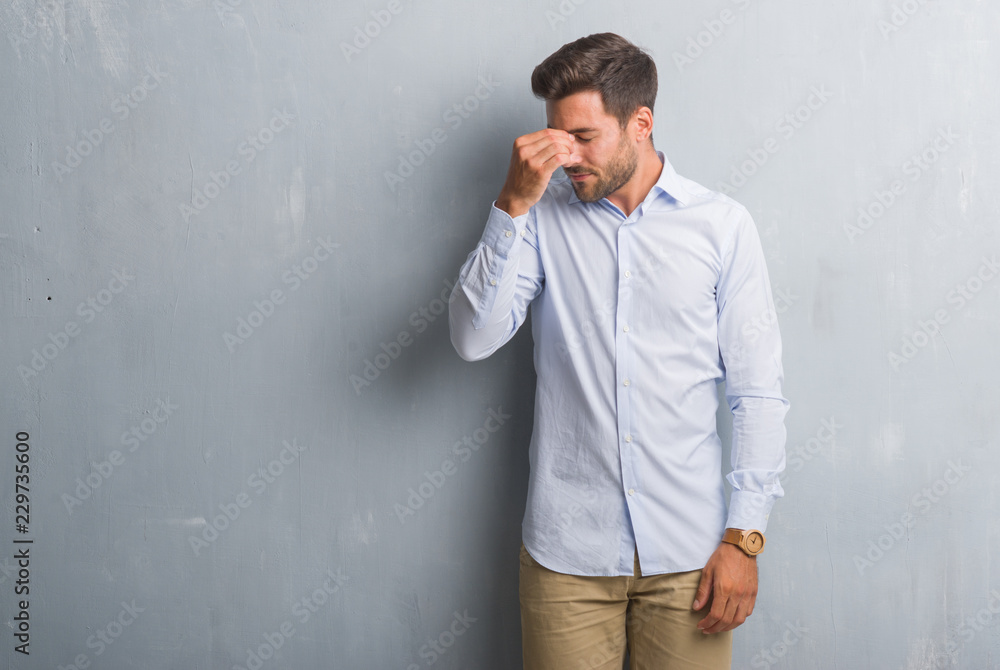 Handsome young business man over grey grunge wall wearing elegant shirt tired rubbing nose and eyes feeling fatigue and headache. Stress and frustration concept.