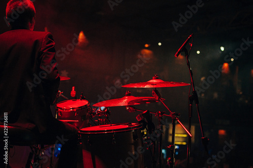 Drummer playing drum set at concert on stage. Music show. Bright scene lighting in club,drum sticks in hands