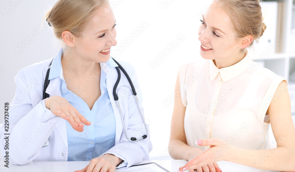 Blonde female doctor and patient talking in hospital office. Health care and client service in medicine Blonde female doctor and patient talking in hospital office. Health care and client service in medicine