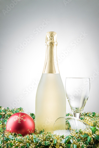 Bottle of champagne, christmas decorations and two glasses on garlands with white gradient background.