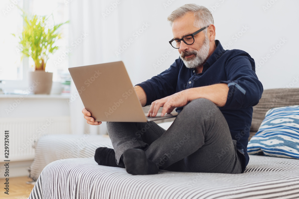 Man sitting cross-legged on a bed with his laptop Man sitting cross-legged on a bed with his laptop