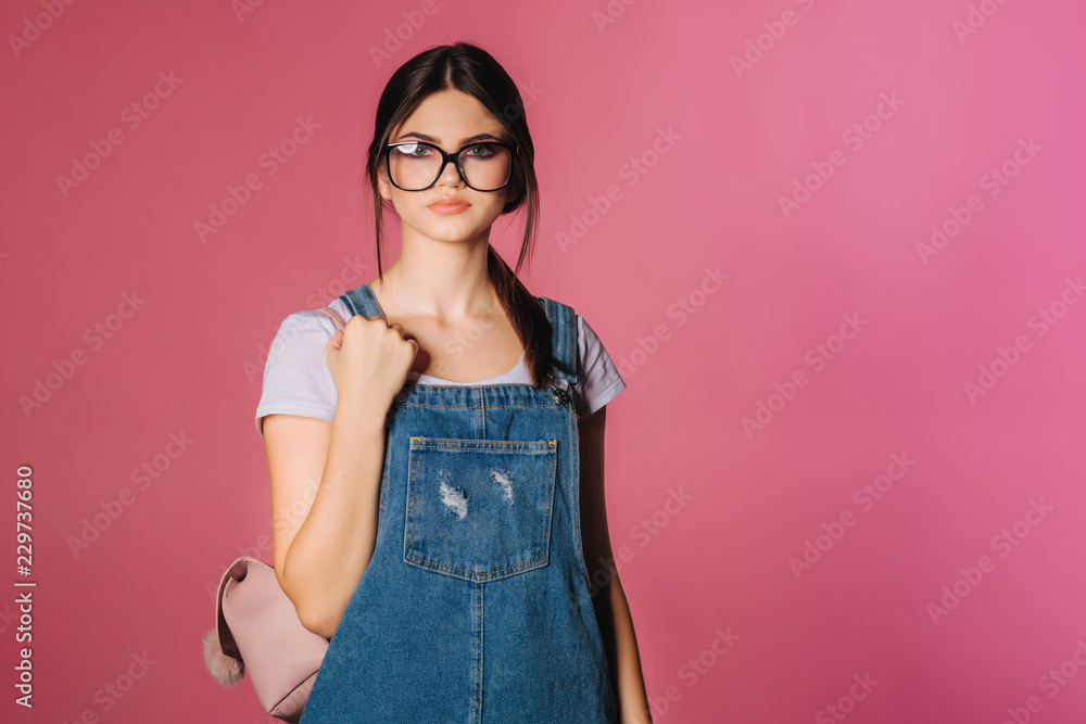 Girl in stylish clothes. Fashion. Trendy charming girl in colorful clothes, wearing black eyeglasses. Accessories. Backpack. Pink background. Fashionable studio of teenage style. Fashionable. Girl in stylish clothes. Fashion. Trendy charming girl in colorful clothes, wearing black eyeglasses. Accessories. Backpack. Pink background. Fashionable studio of teenage style. Fashionable.