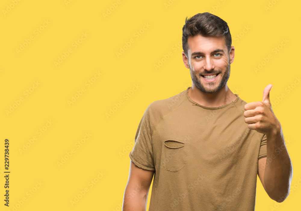Young handsome man over isolated background doing happy thumbs up gesture with hand. Approving expression looking at the camera with showing success. Young handsome man over isolated background doing happy thumbs up gesture with hand. Approving expression looking at the camera with showing success.