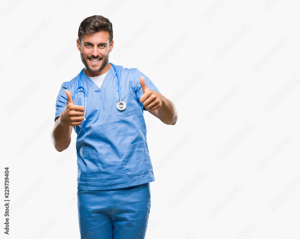 Young handsome doctor surgeon man over isolated background approving doing positive gesture with hand, thumbs up smiling and happy for success. Looking at the camera, winner gesture. Young handsome doctor surgeon man over isolated background approving doing positive gesture with hand, thumbs up smiling and happy for success. Looking at the camera, winner gesture.