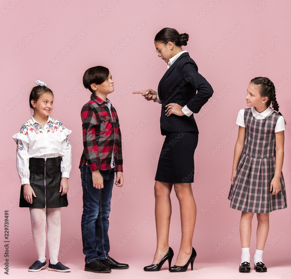 Cute smiling happy stylish children and female teacher on pink background.  Beautiful stylish teen girls and boy standing together and posing at  studio. Classic style. Kids fashion and emotions concept Photos