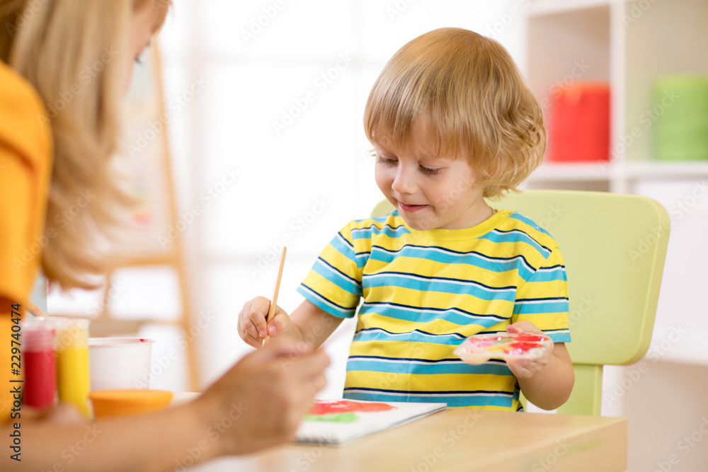 Little child boy painting with teacher in classroom