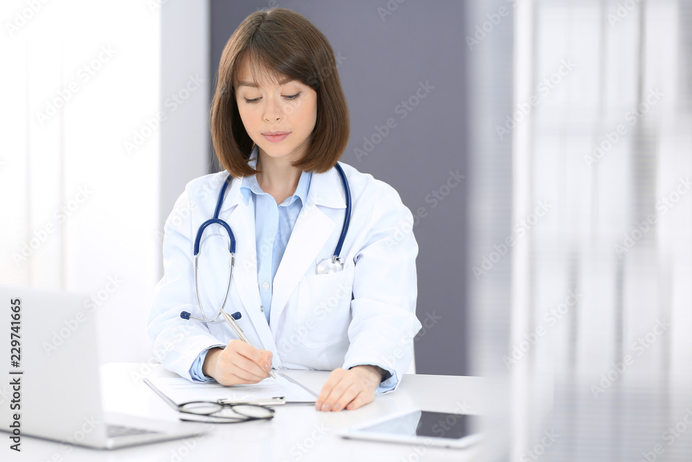 Doctor woman at work. Female physician filling up medical form while sitting the table in clinic or hospital. Medicine and healthcare concept for advertising Doctor woman at work. Female physician filling up medical form while sitting the table in clinic or hospital. Medicine and healthcare concept for advertising