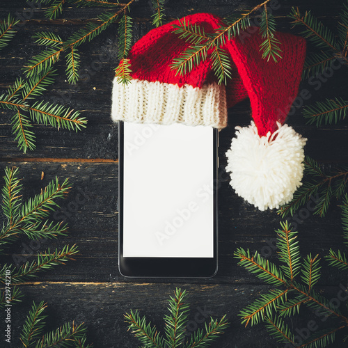 Empty mobile phone with copy space in Christmas hat on dark background with Christmas tree branches