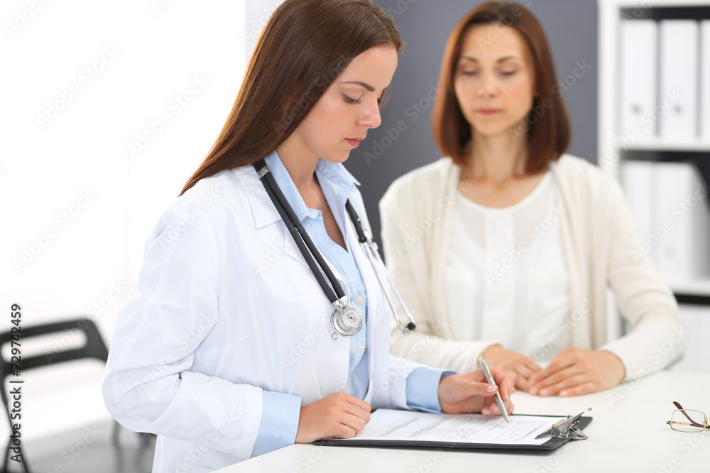 Doctor and patient discussing something while standing near reception desk in emergency hospital. Physician at work in clinic. Medicine and health care concept Doctor and patient discussing something while standing near reception desk in emergency hospital. Physician at work in clinic. Medicine and health care concept
