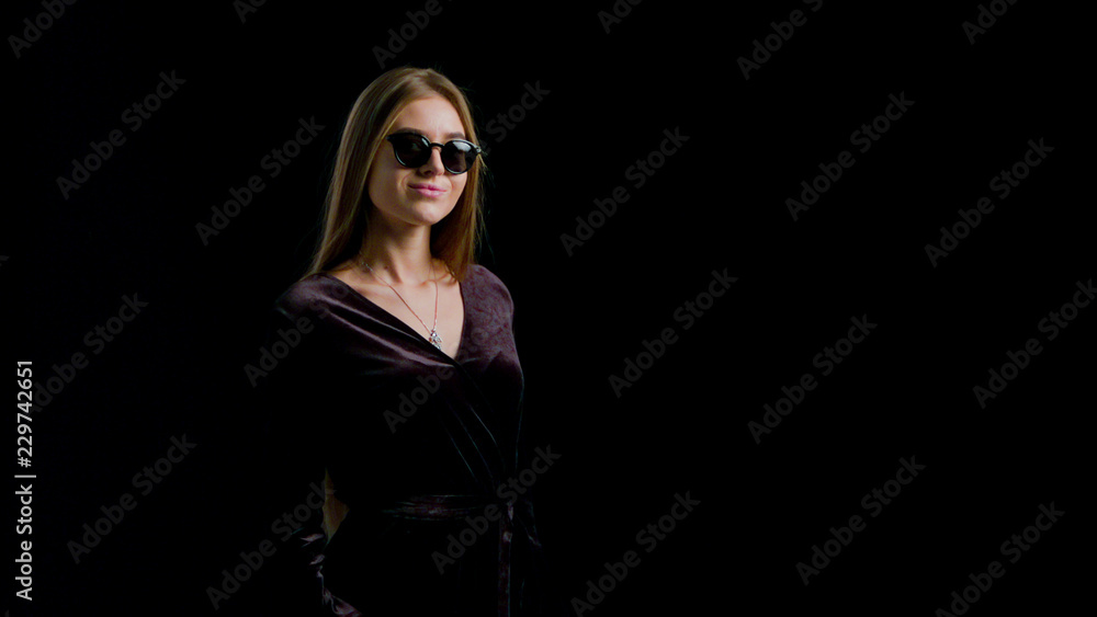 Woman in cool sunglasses and black dress, holding black shopping bag isolated on dark background in black friday holiday or christmas Woman in cool sunglasses and black dress, holding black shopping bag isolated on dark background in black friday holiday or christmas