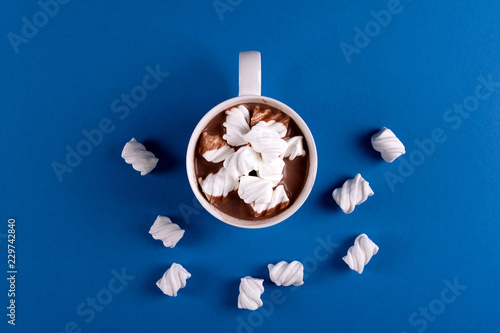 Hot chocolate with marshmallow candies on blue paper background. Top view. Copy space