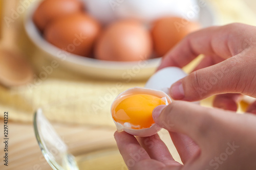 Woman hands breaking an egg to separate egg white and yolks, egg shells at the background