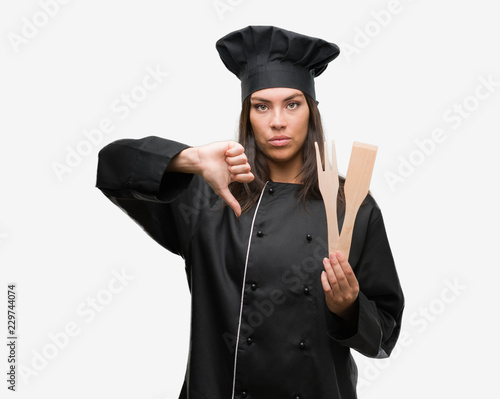 Young hispanic cook woman wearing chef uniform with angry face, negative sign showing dislike with thumbs down, rejection concept