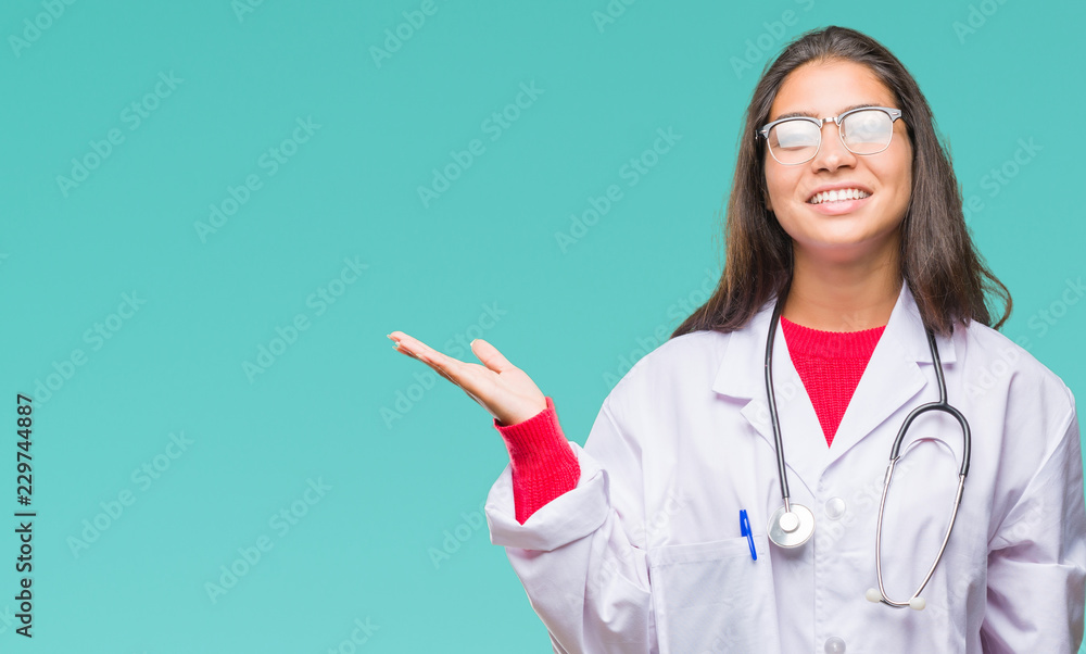 Young arab doctor woman over isolated background smiling cheerful presenting and pointing with palm of hand looking at the camera. Young arab doctor woman over isolated background smiling cheerful presenting and pointing with palm of hand looking at the camera.
