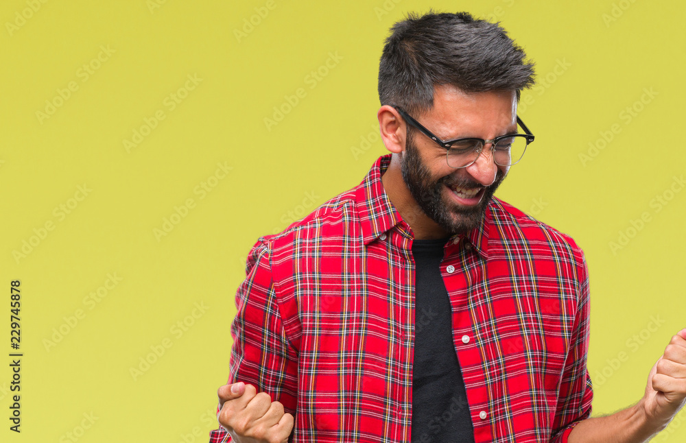 Adult hispanic man wearing glasses over isolated background very happy and excited doing winner gesture with arms raised, smiling and screaming for success. Celebration concept. Adult hispanic man wearing glasses over isolated background very happy and excited doing winner gesture with arms raised, smiling and screaming for success. Celebration concept.