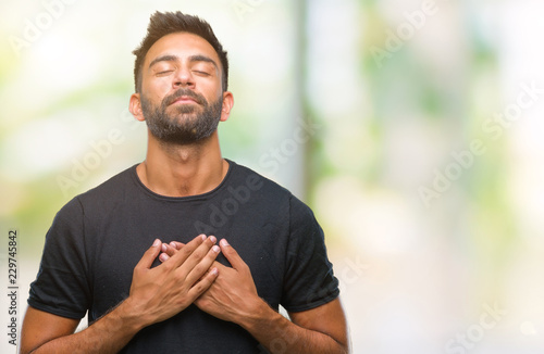 Фотография Adult hispanic man over isolated background smiling with hands on chest with closed eyes and grateful gesture on face