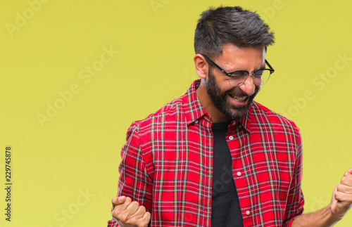 Adult hispanic man wearing glasses over isolated background very happy and excited doing winner gesture with arms raised, smiling and screaming for success. Celebration concept.